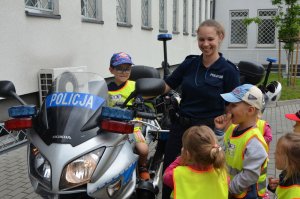 Dzieci z przedszkola oglądają policyjny motocykl na parkingu komendy.