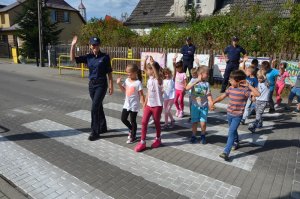 Policjanci uczą dzieci bezpiecznego przechodzenia przez przejście dla pieszych.