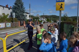 Policjantka uczy dzieci przechodzić przez jezdnię przez przejście dla pieszych w rejonie szkoły.