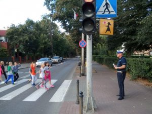 Policjant ruchu drogowego uczy dzieci jak bezpiecznie iść do szkoły.