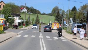 Miejsce zdarzenia, na którym widać po prawej stronie stojący radiowóz, po lewej natomiast karetkę pogotowia, stojących przechodniów, motocykl stojący przy karetce a na drodze na wprost stoi wóz straży pożarnej.