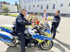 Policjant siedzi na motocyklu i rozmawia z dziećmi, obok stoi także policjantka