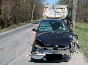 Miejsce zdarzenia drogowego na drodze wojewódzkiej W 218 oraz widoczny rozbity przód samochodu osobowego oraz w tle tył samochodu ciężarowego.