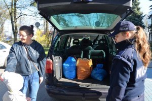 Policjantka stoi przy samochodzie osobowym razem z mamą Nikodema oraz jego młodszym bratem, w otwartym samochodzie w bagażniku stoją worki z plastikowymi nakrętkami.