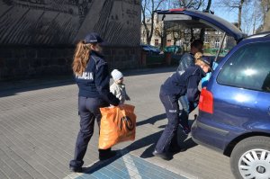 Policjantki niosą torby z nakrętkami do samochodu, wkładają je do otwartego bagażnika w pojeździe.