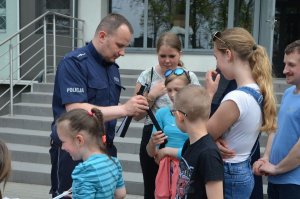 Policjant przed budynkiem KPP Wejherowo rozdaje dzieciom odblaskowe opaski