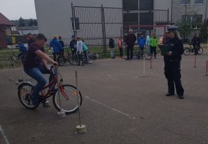 Policjantka nadzoruje przebieg konkurencji praktycznych - jazda rowerem po torze przeszkód.