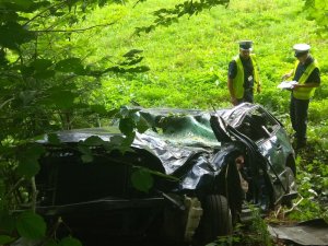 Policjanci wykonują oględziny rozbitego samochodu.