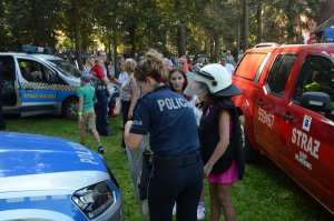 Policjantka pomaga dziecku ubrać umundurowanie ćwiczebne przy radiowozie