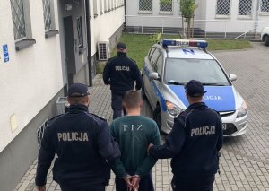 Policjanci prowadzą zatrzymanego do radiowozu.