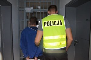 Policjant prowadzi zatrzymanego mężczyznę do pomieszczenia dla osób zatrzymanych.