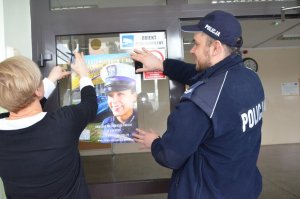 Dzielnicowy wspólnie z Panią dyrektor wywiesza plakat dotyczący naboru do służby w Policji