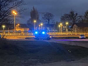 Radiowóz przejeżdżający w porze nocnej na sygnałach po nieutwardzonym parkingu