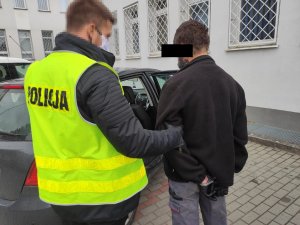 Policjant prowadzi zatrzymanego do radiowozu.