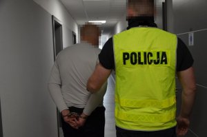 Policjant prowadzi zatrzymanego mężczyznę po korytarzu