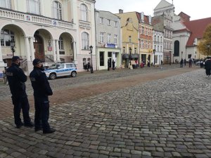 Policjanci zabezpieczali protest na Placu Wejhera. NA zdjęciu widać dwóch policjantów, w oddali policyjny radiowóz i osoby które protestują