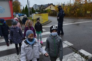 Policjant nadzoruje jak grupa pierwszoklasistów przechodzi przez przejście dla pieszych