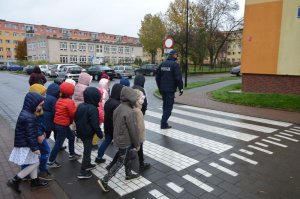 Pierwszoklasiści podążają za policjantem na przejściu dla pieszych