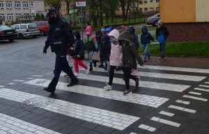 Pierwszoklasiści podążają za policjantem na przejściu dla pieszych