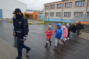 Pierwszoklasiści podążają za policjantem na przejściu dla pieszych