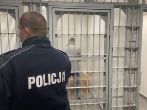 dzielnicowy stoi przed celą z zatrzymanym, który stoi tyłem do drzwi w środku