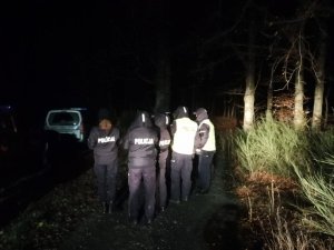 policjanci szukają zaginionego , na zewnątrz jest ciemno, rejon leśny