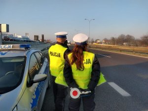 Dwoje policjantów stoi przodem do nienadjeżdżających samochodów, policjant po lewej wykonuje pomiar prędkości