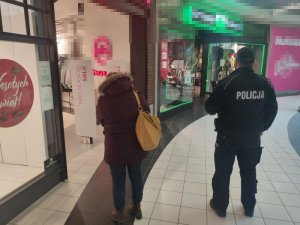 Policjant z pracownikiem sanepidu przeprowadzają kontrolę w galerii handlowej idą korytarzem