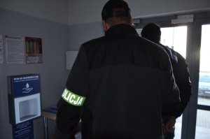 Policjant prowadzi zatrzymanego do wyjścia z budynku