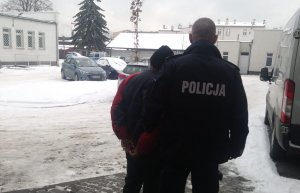 Policjanci prowadzą zatrzymanego mężczyznę do radiowozu