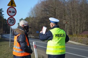 Policjant oraz członkowie komisji rozmawiają na miejscu wypadku i sprawdzają infrastrukturę drogową.