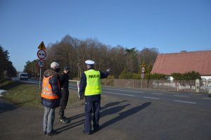 Policjant oraz członkowie komisji rozmawiają na miejscu wypadku i sprawdzają infrastrukturę drogową.