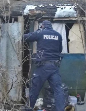 Policjant wchodzi do małego domku, zbitego z desek, wyglądającego jakby miał się rozpaść