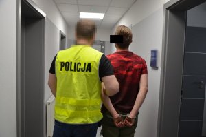 Policjant prowadzi zatrzymanego mężczyznę wewnątrz budynku, korytarzem.