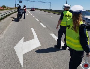 Policjantka z policjantem stoją na drodze, a za nimi stoi dwóch motocyklistów