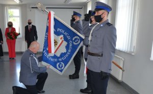 Komendant klęka przed sztandarem, przed nim stoją trzej policjanci