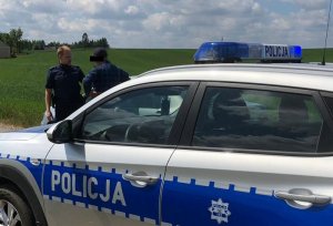 Za radiowozem stoi policjant, który rozmawia z innym mężczyzną.