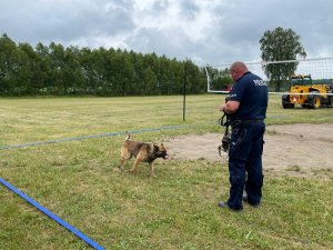 Policjant stoi na przeciwko idącego w jego kierunku psa. Widać że pies otrzymał komendę.