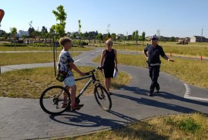 Policjant wspólnie z nauczycielem chodzi po placu, przy rowerzyście