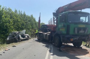 Pomiędzy samochodem ciężarowym a osobowym stoi policjant, który rozmawia ze strażakami.