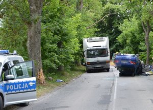 Samochód leży na dachu, w tle na pierwszym planie widać policyjny radiowóz, a za samochodem który leży na dachu widać samochód dostawczy