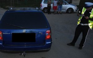 Policjant stoi po prawej stronie granatowego volkswagena, sporządza dokumentację.