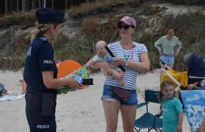 Policjantka rozmawia z kobietą, która trzyma niemowlę na rękach.