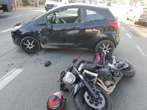 Widoczny jest lewy pok samochodu ford z rozbitą szybą a tuż obok leży, wywrócony na bok motocykl.