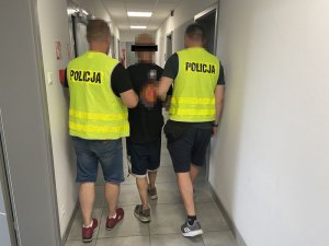 Policjanci prowadzą zatrzymanego mężczyznę.