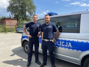 Dwaj policjanci w mundurach stoją na tle radiowozu