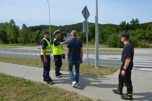 Czteroosobowa komisja rozmawia na miejscu wypadku, ustala okoliczności, jeden z policjantów coś pokazuje ręką