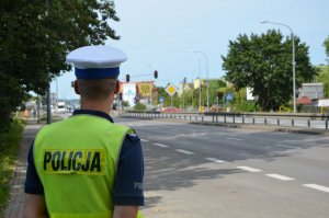 Policjanci stoi przy drodze, przygląda się przejeżdżającym samochodom.