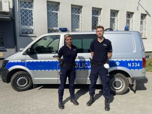 Dwoje policjantów stoi na tle policyjnego radiowozu.