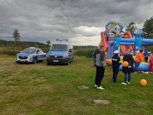 Policjantka stoi i rozmawia z uczestnikiem festynu, w tle policyjne radiowozy i dmuchana zjeżdżalnia.